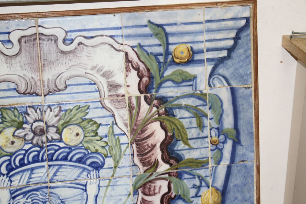 A Continental maiolica tile panel, depicting a putto holding aloft a basket of fruit, overall 90 x 72cm